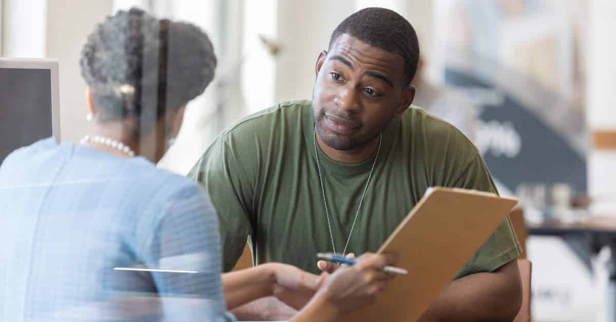 Young man talking to a woman who is holding a clipboard and explaining something.