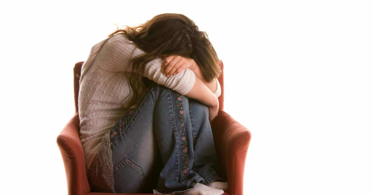 Teen girl with her head down and her arms wrapped around her knees.