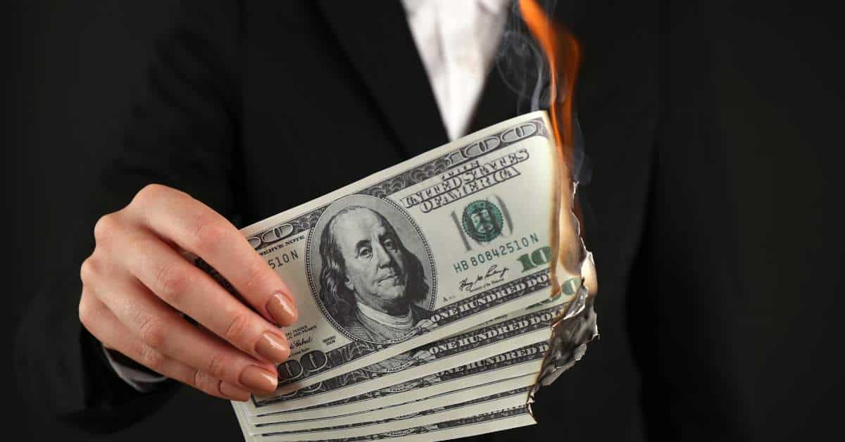 Someone holding a stack of $100 bills that are on fire
