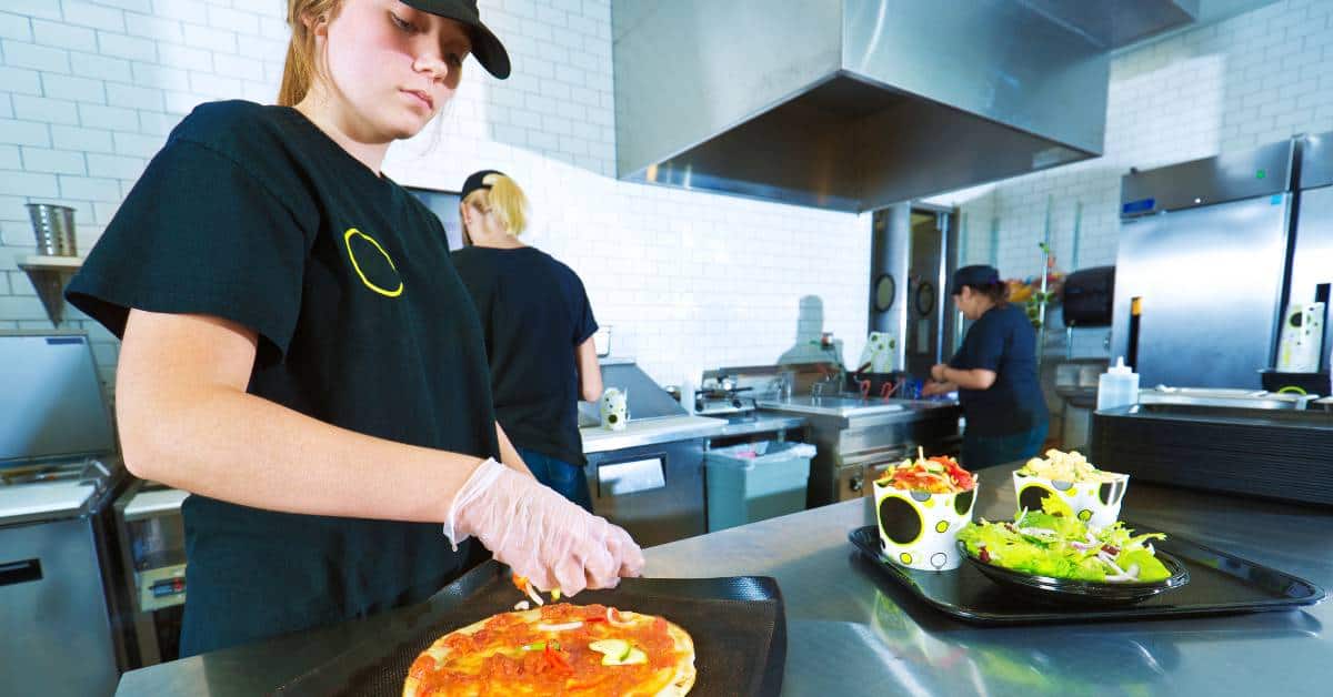 Teenage girl making a pizza working at a pizza restaurant.
