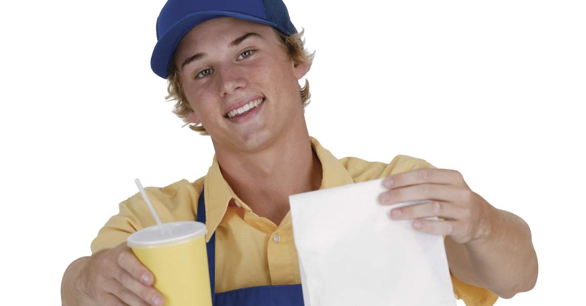 Young man working at a fast food restaurant handing a customer a drink and a bag of food