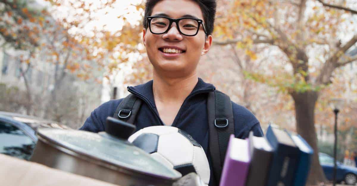 Smiling young man carrying boxes as he moves into his dorm