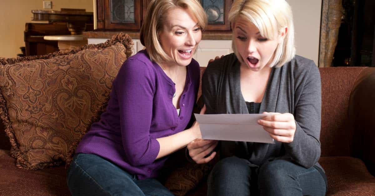Mother and daughter sitting on a couch excitedly exclaiming over a letter the daughter holds