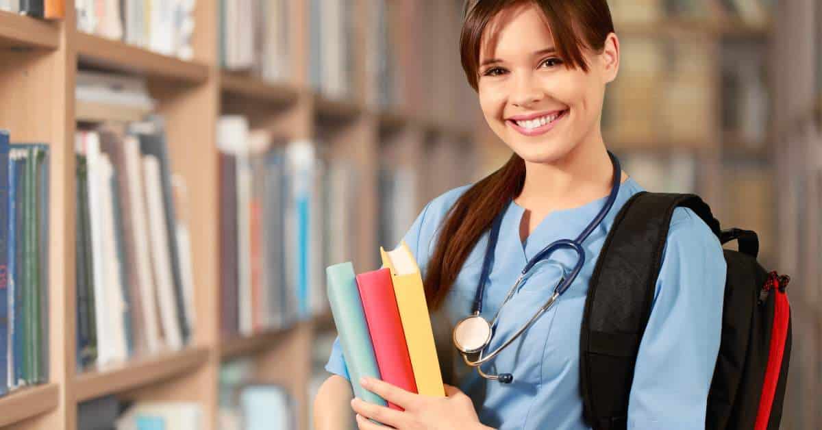 Female student holding books. She has a stethoscope around her neck and is wearing scrubs.