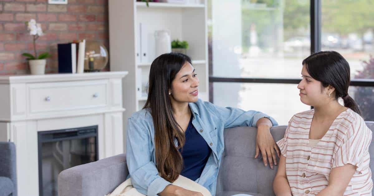 Mother sitting on the couch with her teen child talking.