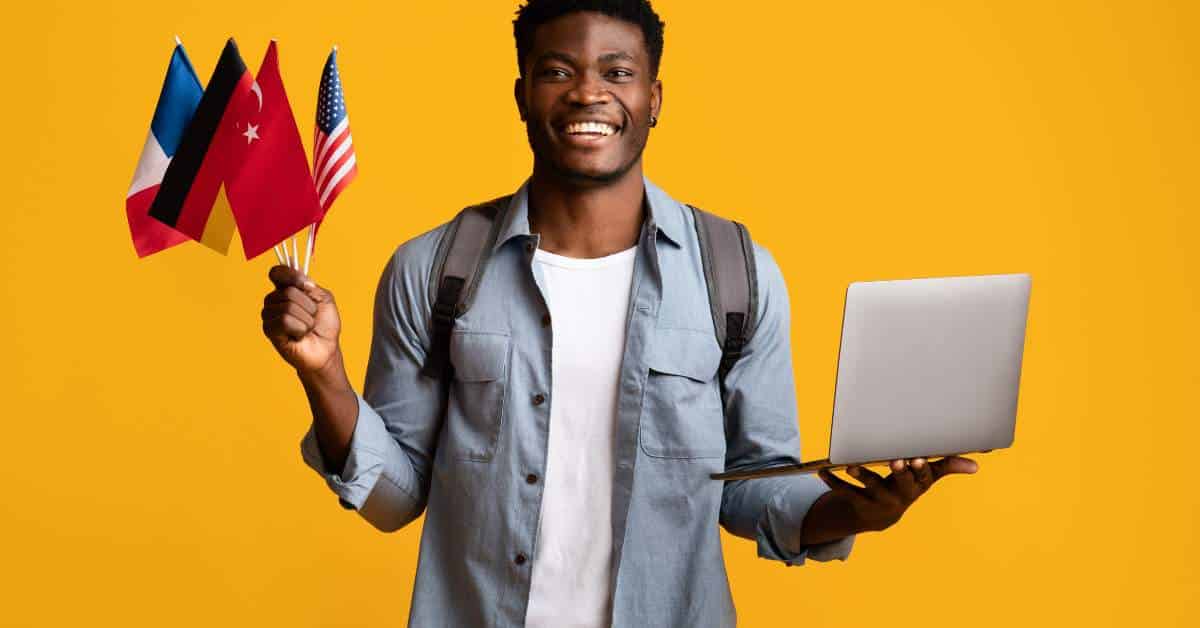 Young man holding a computer in one hand and flags from several countries in the other.