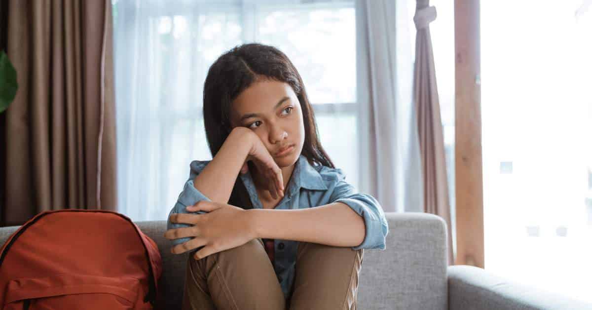 Teen girl sitting on the couch looking dejected.