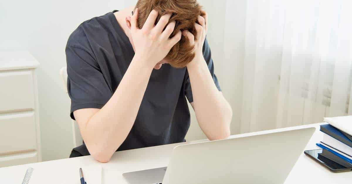 Teen boy sitting at his computer desk, dejected with his head in his hands