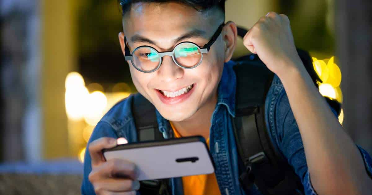 Teen man gleefully looking at his phone while raising a fist in triumph