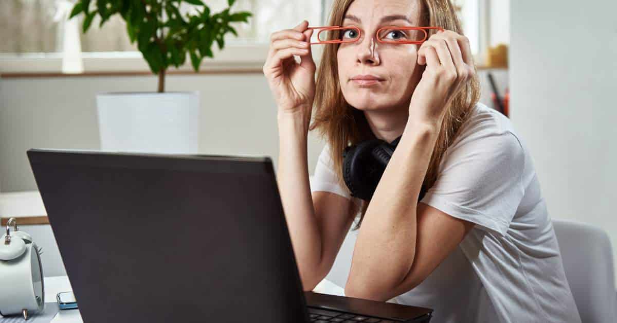 Bored teen girl looking up from her computer and holding large paperclips in front of her eyes like glasses.