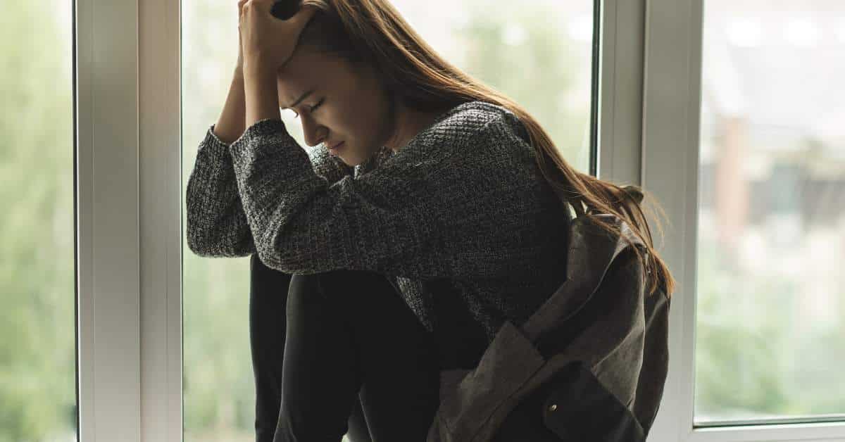 Teen girl sits depressed with hands on forehead