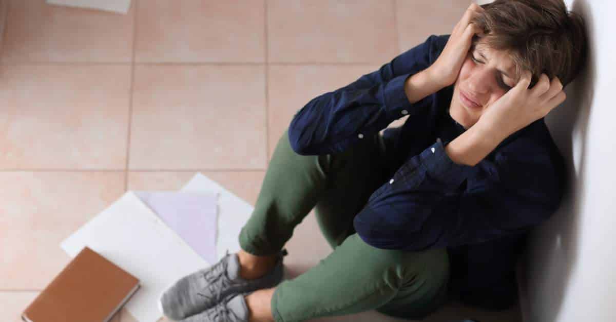 Teen huddled on the bathroom floor with notebooks spread around him and his hands clenched around his head