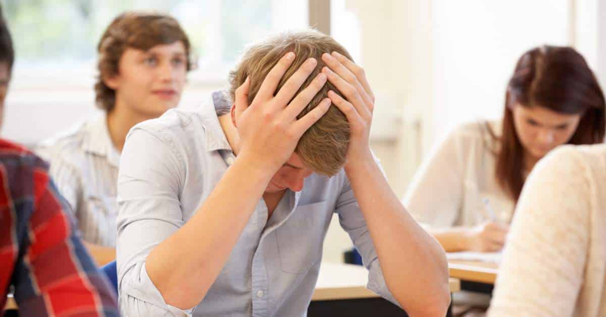 Teen boy sitting with his head in his hands in the middle of a classroom