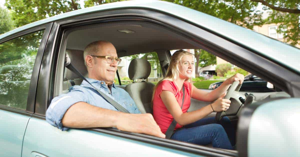 Female teen driver at the wheel of a car with her father in the passenger seat.