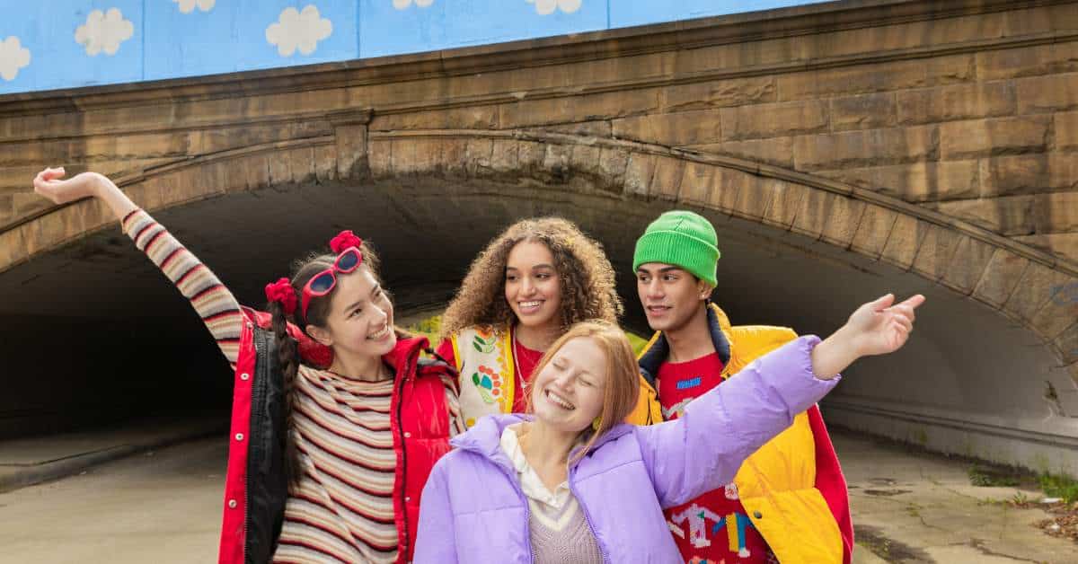 One male and three female teens posing for a picture with their arms outstretched