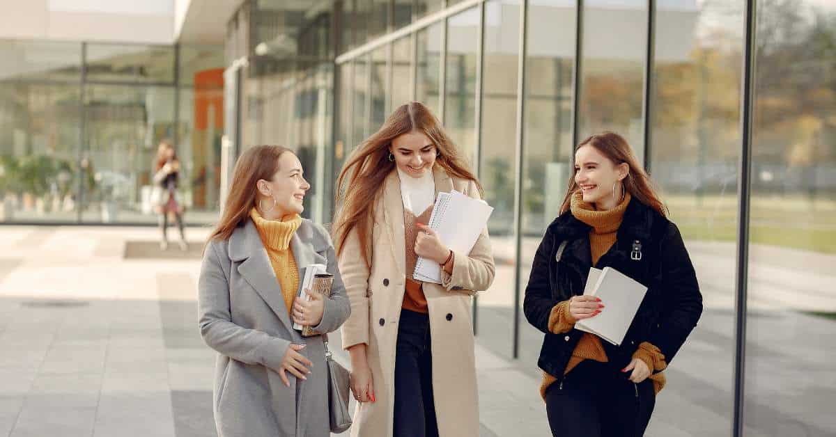 Three girls walking outside next to a college building