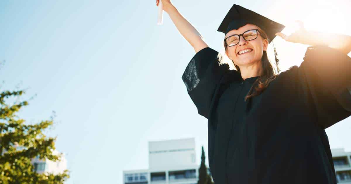 Teen in a graduation gown raising her arm in excitement and success