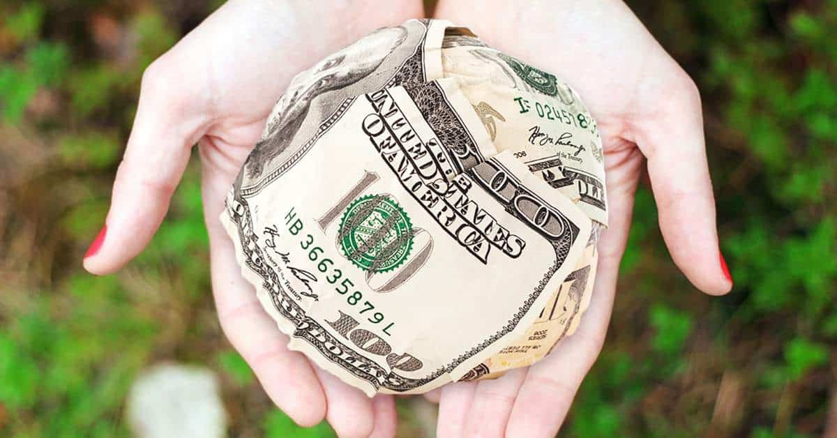 Woman holding out cupped palms with crumpled $100 bills inside.