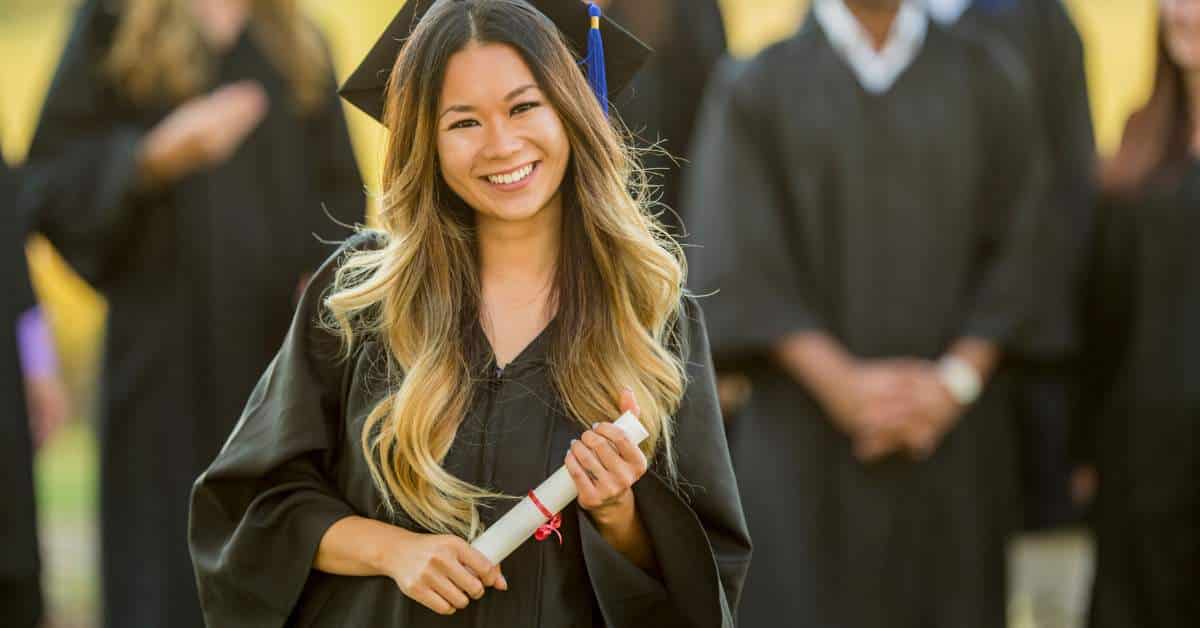 Smiling Asian woman wearing a cap and gown holding a dipoloma
