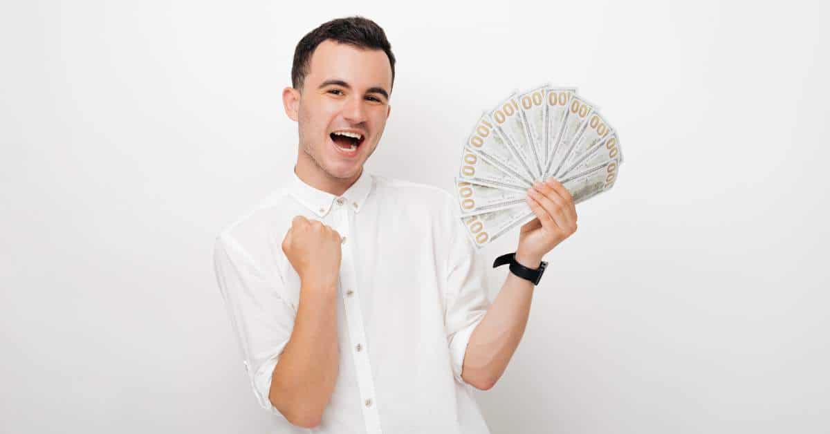 Young man pumping one fist and holding a fan of cash in the other.