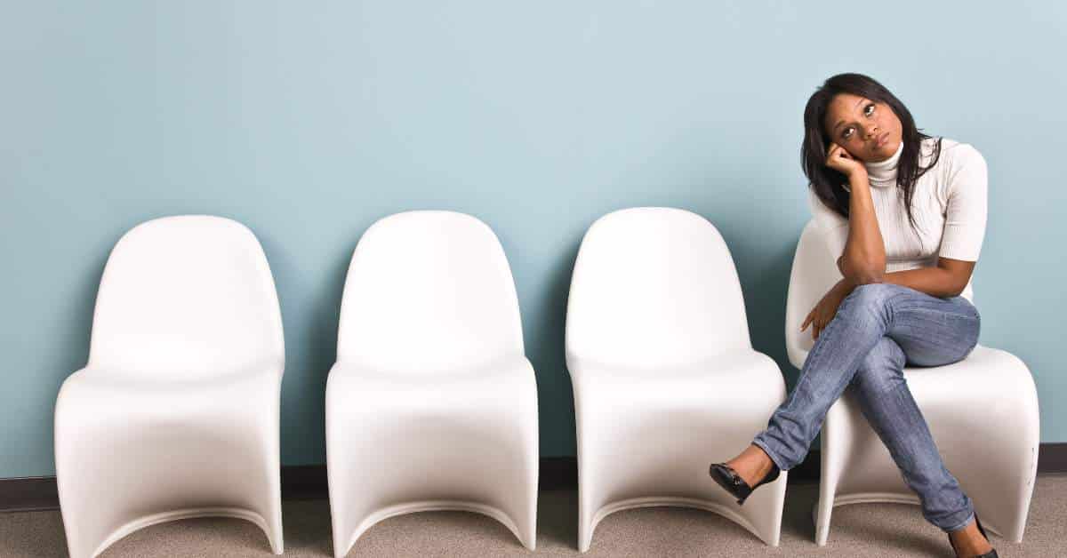 Young woman sitting in a chair in a waiting room looking board