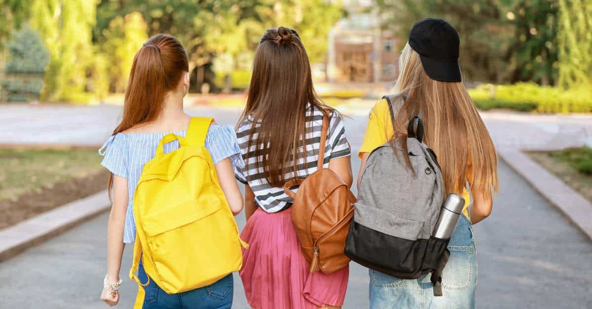Three teen girls walking away from the camera with backpacks slung over their shoulders.