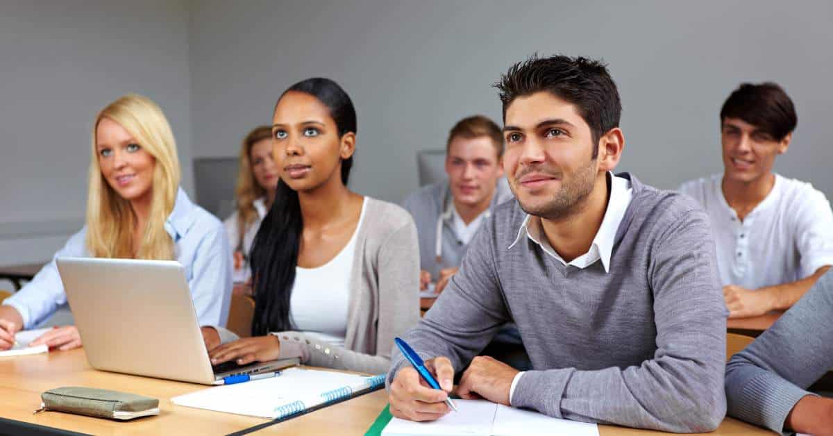 Three high school/college students sitting in a classroom looking up at the teacher
