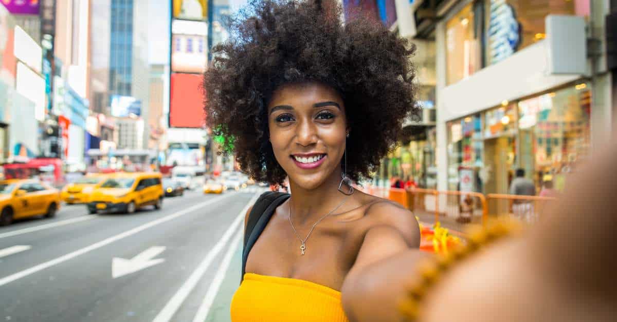 Woman in a yellow dress taking a selfie with a NYC street in the background