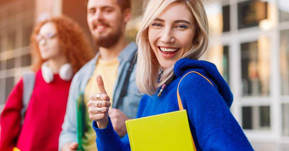 Happy college student turns sideways toward the camera and holds her thumb up.