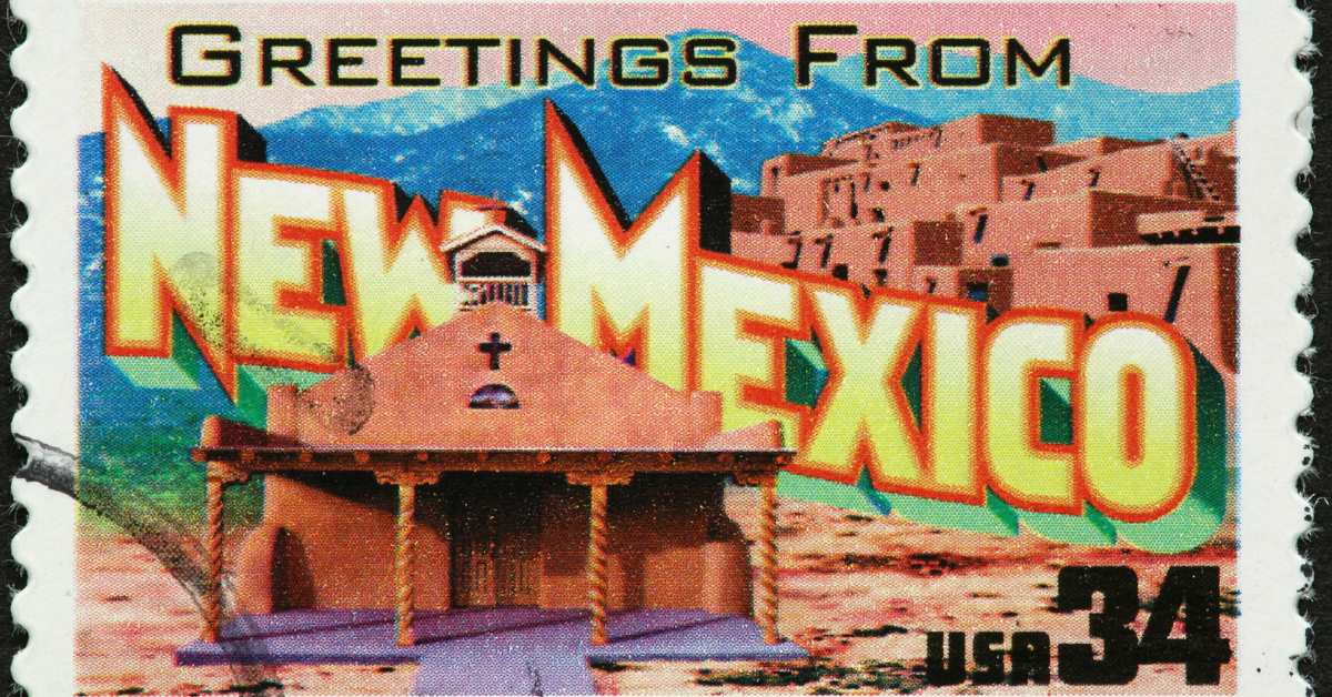 Picture of a postal stamp with an adobe church on the front and "Greetings from New Mexico" written on it.