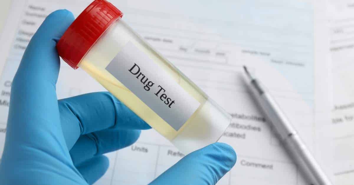 The hand of a person in blue lab gloves holding a vial that says, "Drug Test"