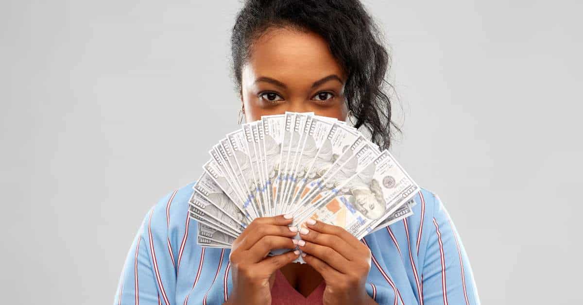 African American woman holding a fan of money in front of her face.